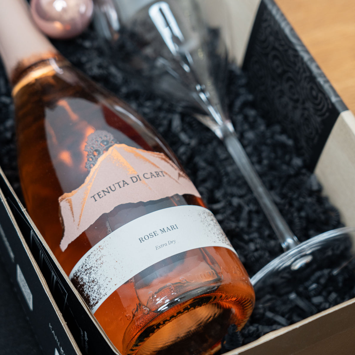 Prickelnder Rosé-Gruß mit Glas – geöffnetes Geschenkpaket